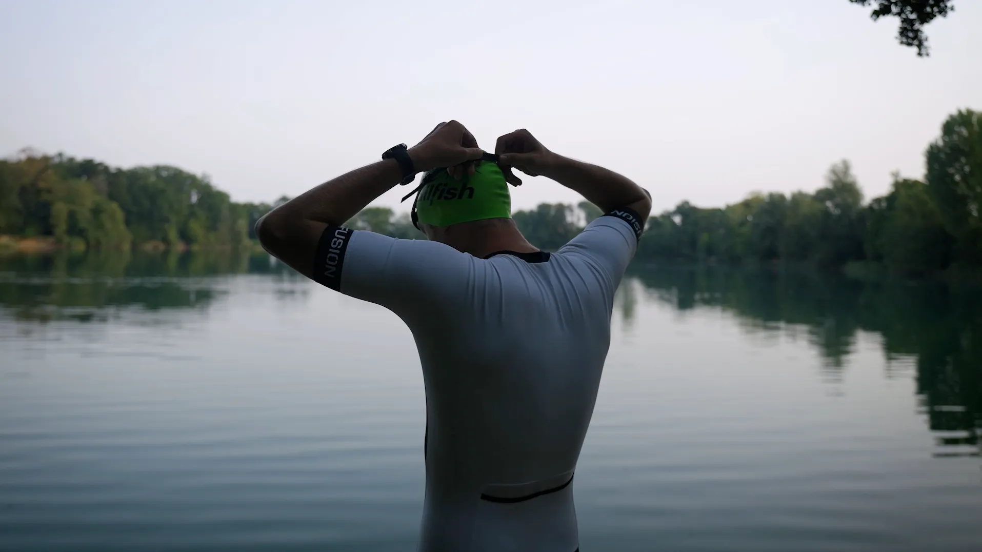 Pascal Kayser im Triathlonanzug setzt vor dem Schwimmen am See die Badekappe auf, von hinten gesehen