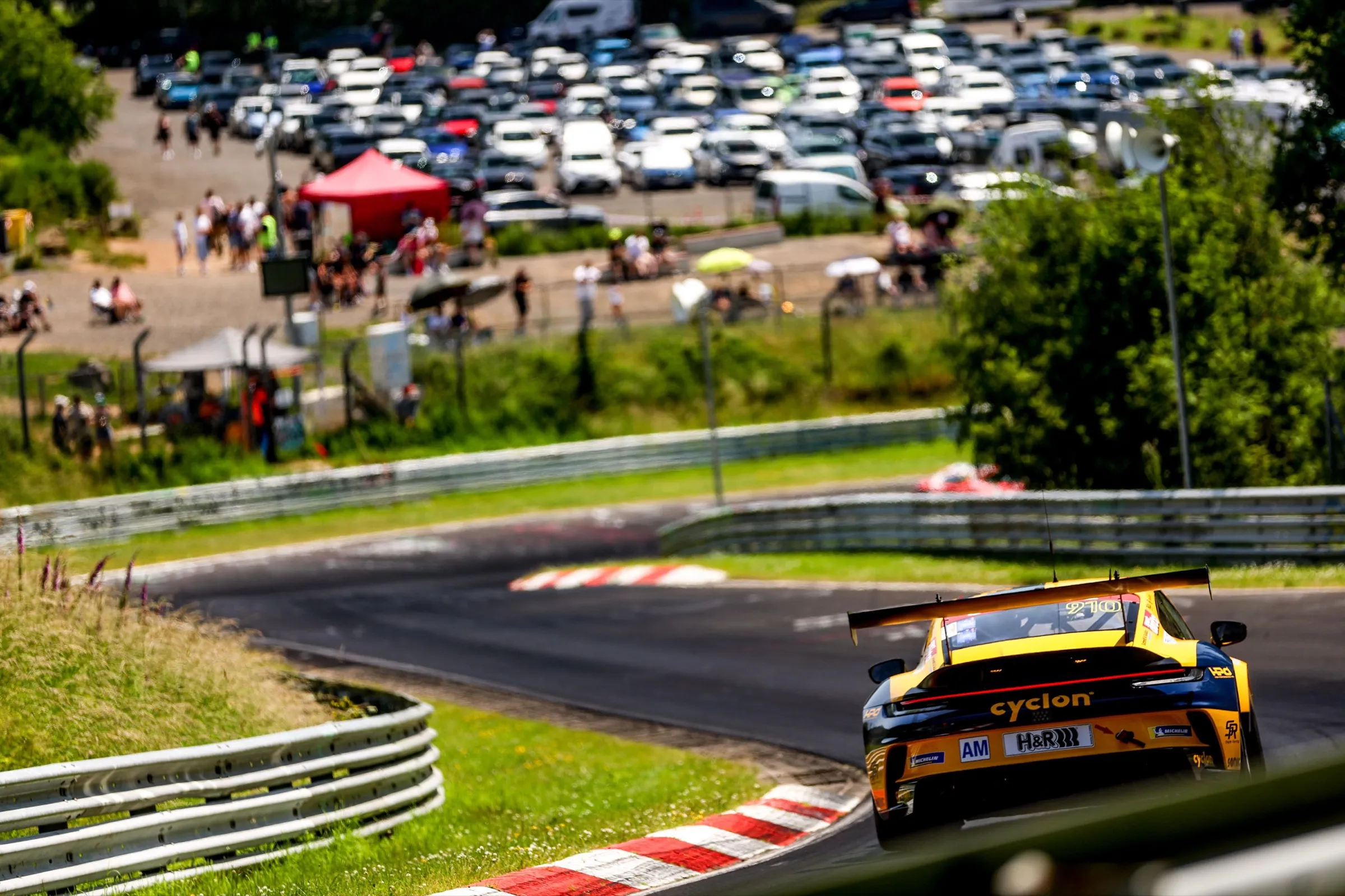 Gelber Rennwagen von hinten auf der Nordschleife, im Hintergrund Zuschauer am Streckenrand