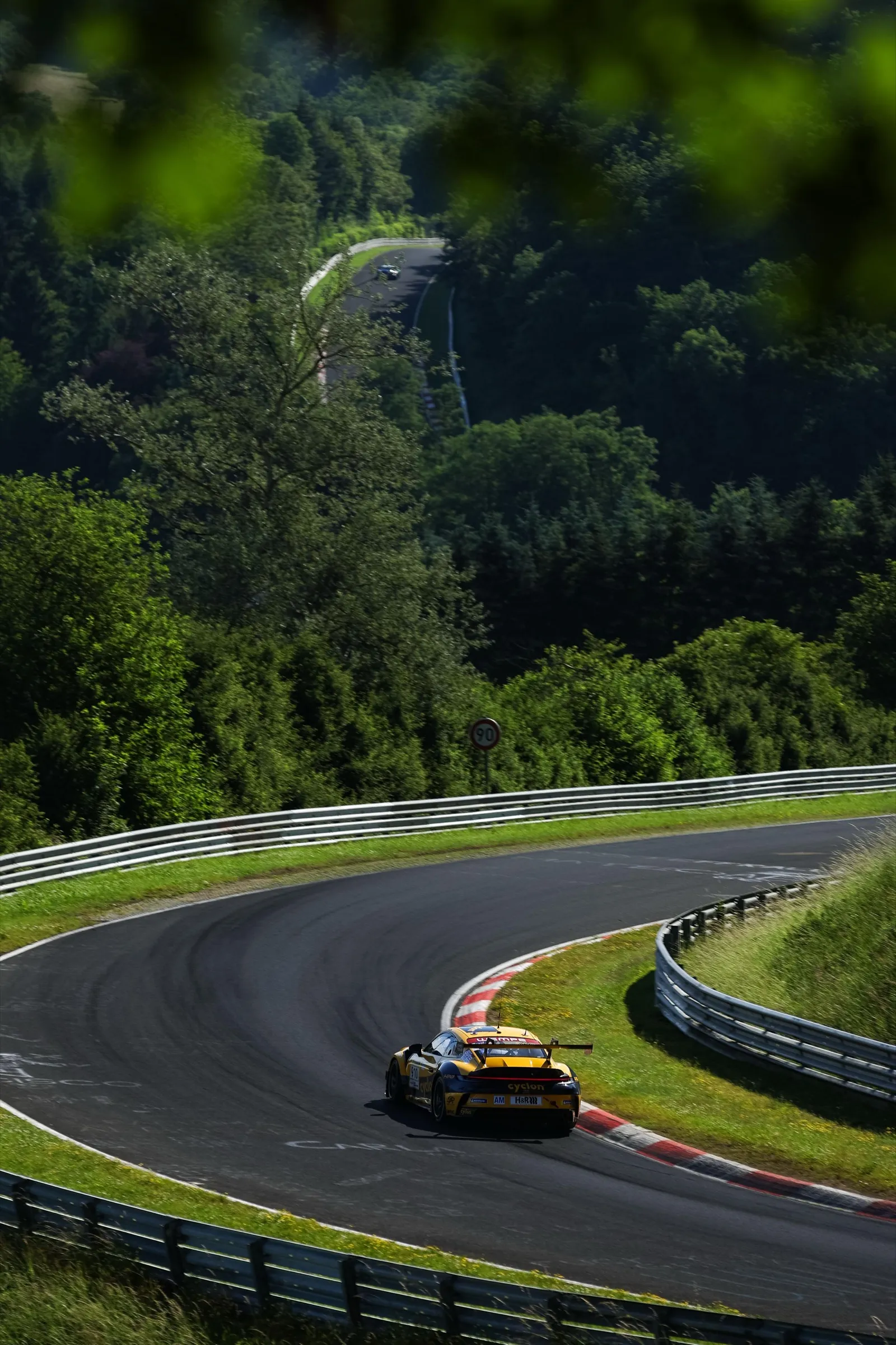 Gelber Rennwagen in einer Kurve der Nordschleife am Nürburgring, rundherum dichter Wald