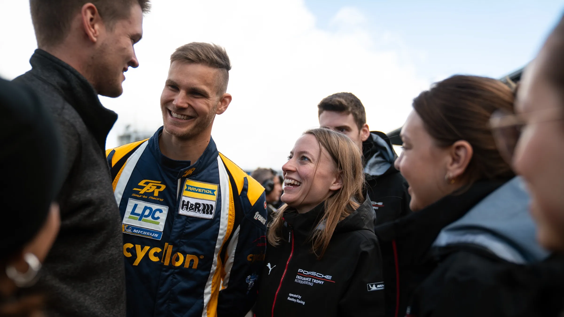 Pascal Kayser im Gespräch mit einem lachenden Fahrer von Smyrlis Racing, umringt von weiteren Menschen