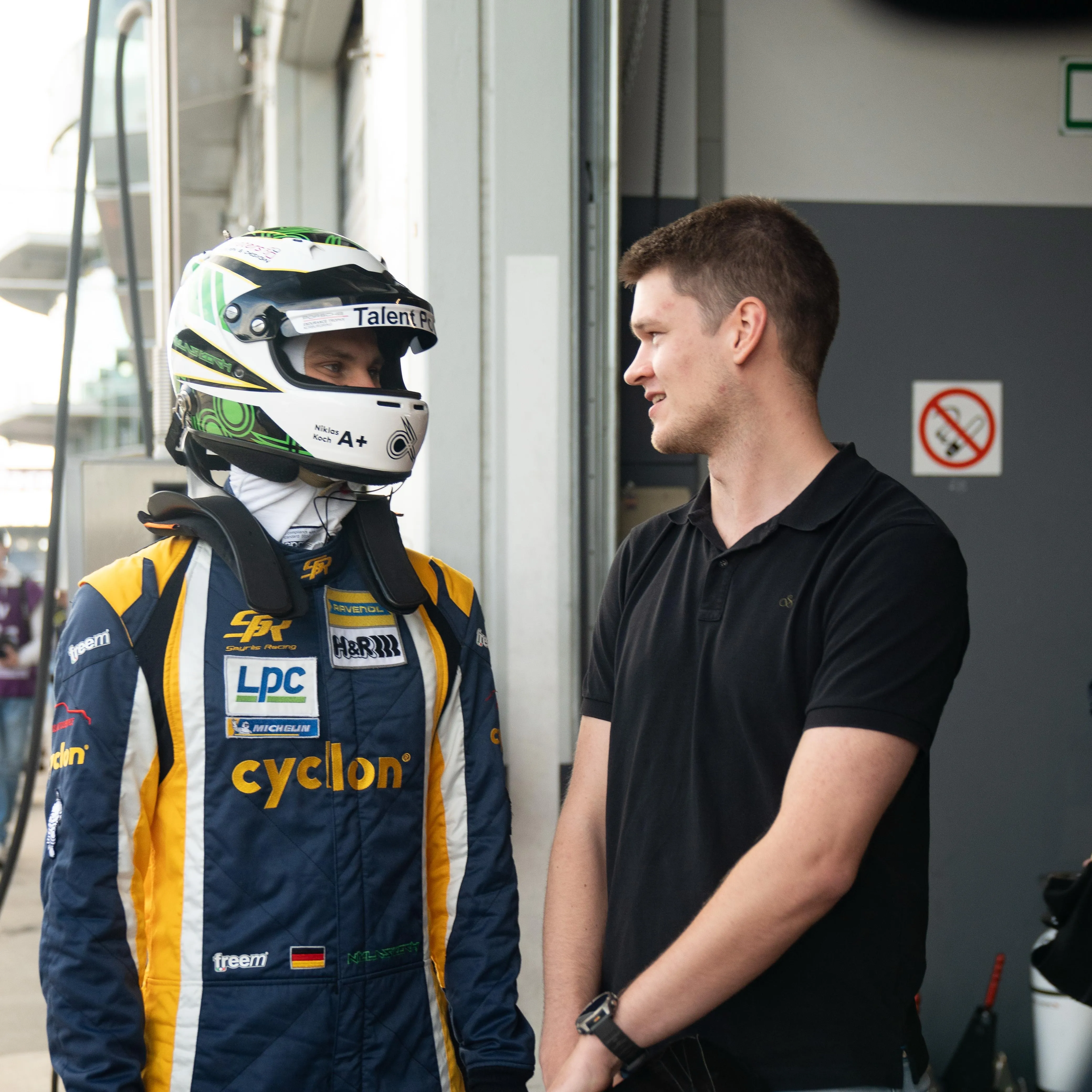 Pascal Kayser im Gespräch mit Rennfahrer Niklas Koch in Rennanzug und Helm an der Box der Nürburgring Langstreckenserie