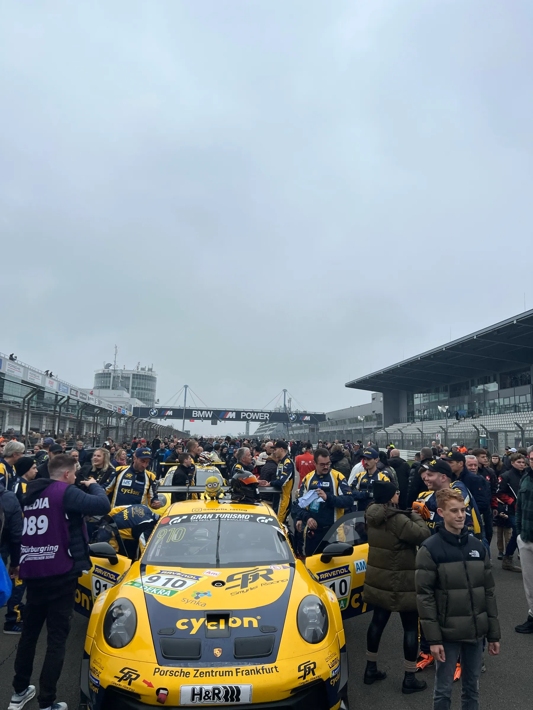 Startaufstellung am Nürburgring: der gelbe Porsche mit der Startnummer 910 zwischen Team und Zuschauern