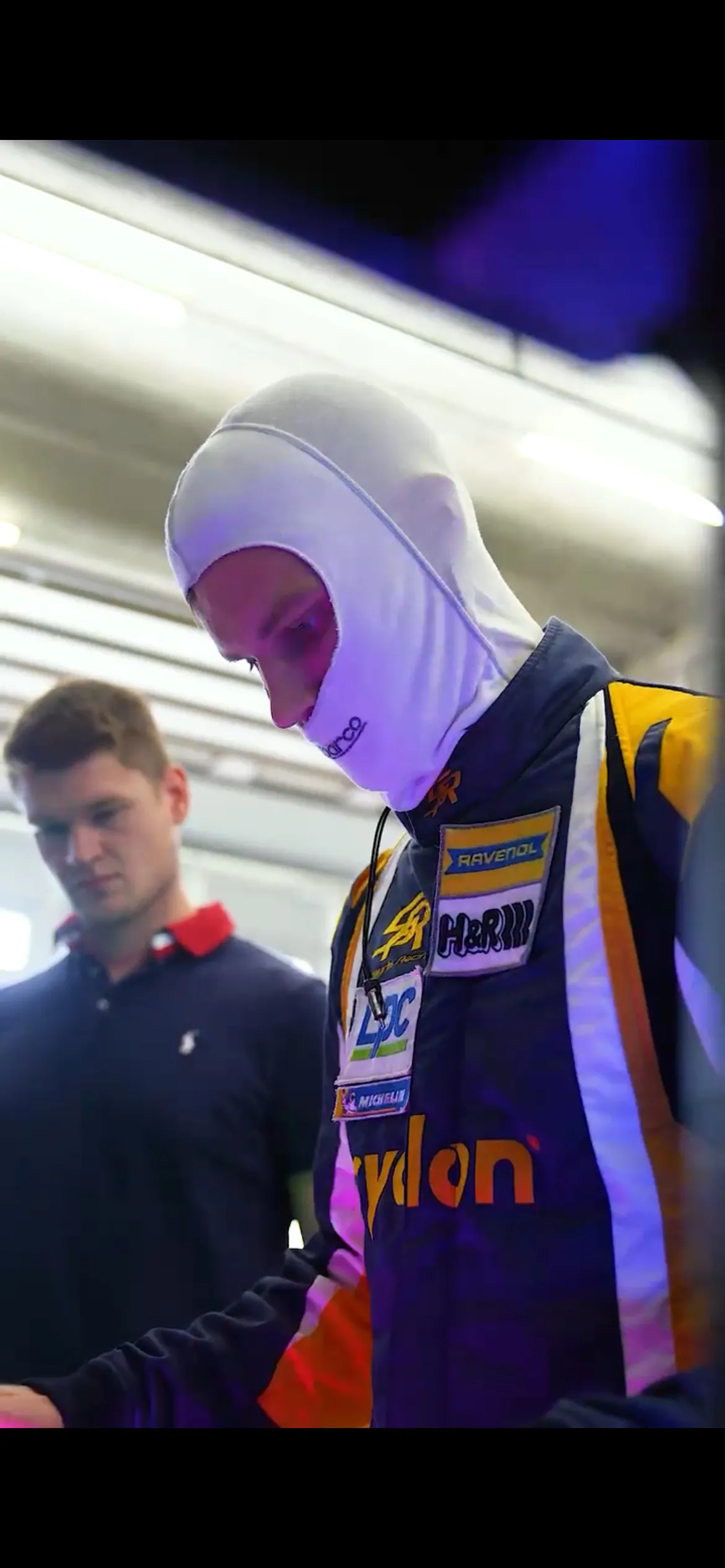 Fahrer von Smyrlis Racing in Rennanzug und Sturmhaube in der Box, Pascal Kayser beobachtet ihn von der Seite